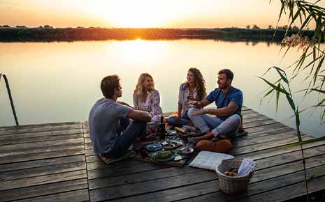 group of friends sitting on lakeside dock having picknic at sunset